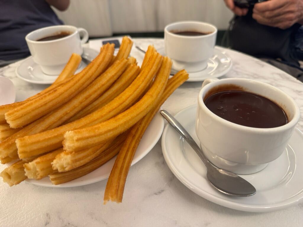 Ein Teller Churros und drei Tassen hei&szlig;e Schokolade auf Marmor